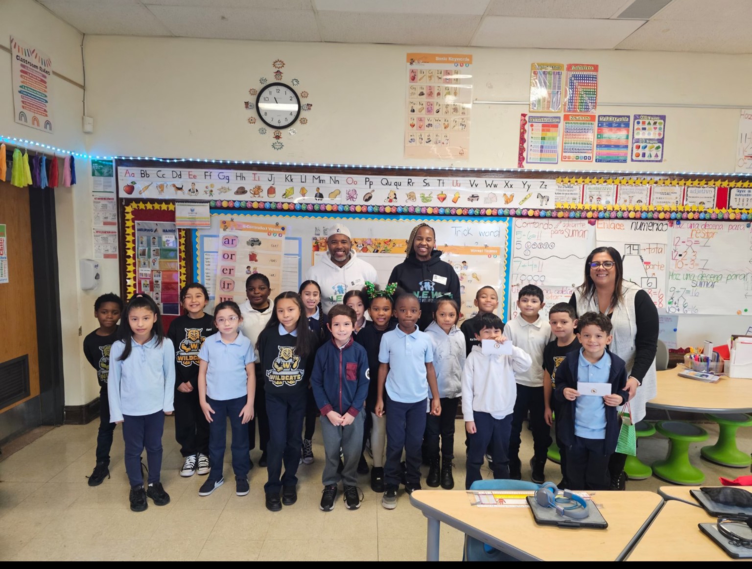 Coach T and Coach J standing with a group of children and their teacher in a classroom