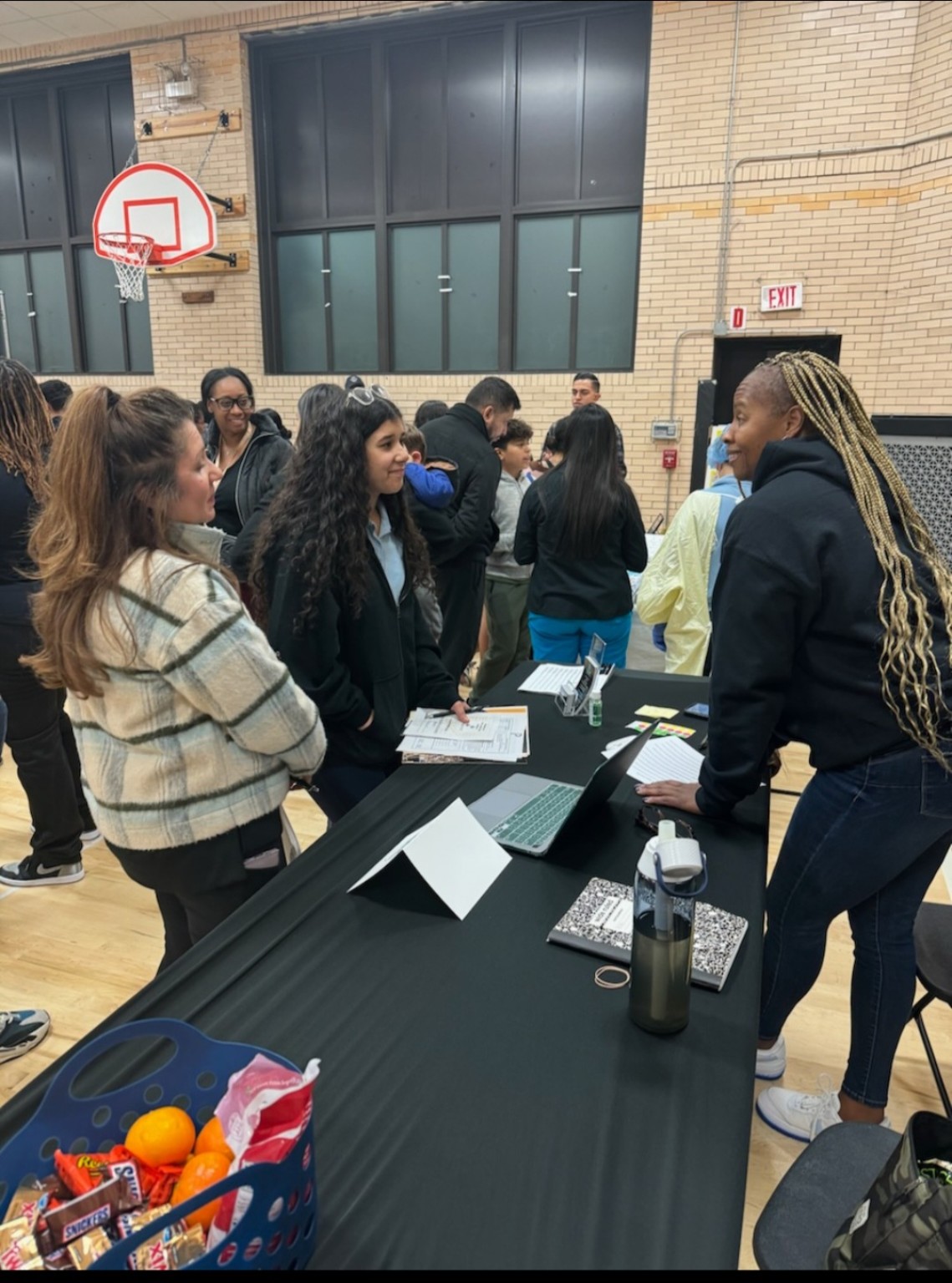 Coach T talking with two young people beside an information table in a school gym