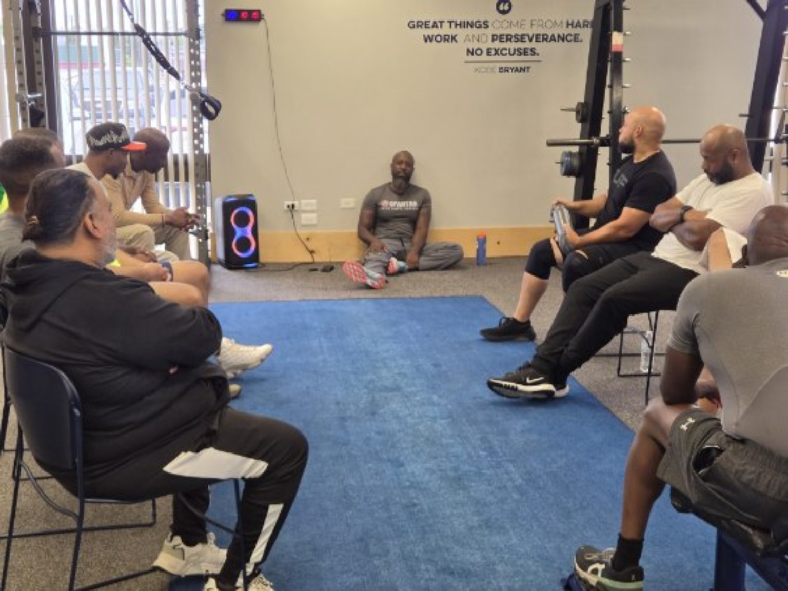 Men seated around a blue mat in the gym during a Sanctuary conversation