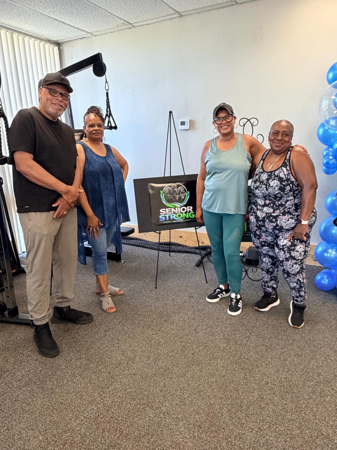 Four adults smiling beside a Senior Strong display in the fitness studio